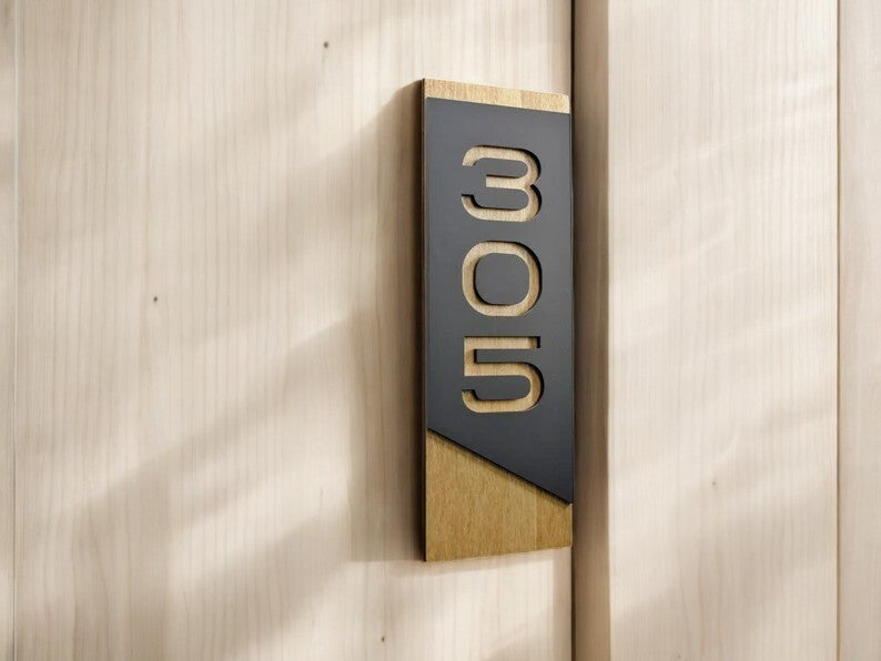 A tall house number plaque mounted flat on light exterior wall cladding